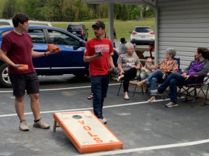 Cody and Thomas playing cornhole. Leta, Kaylee, Sheila, and Cara talking.